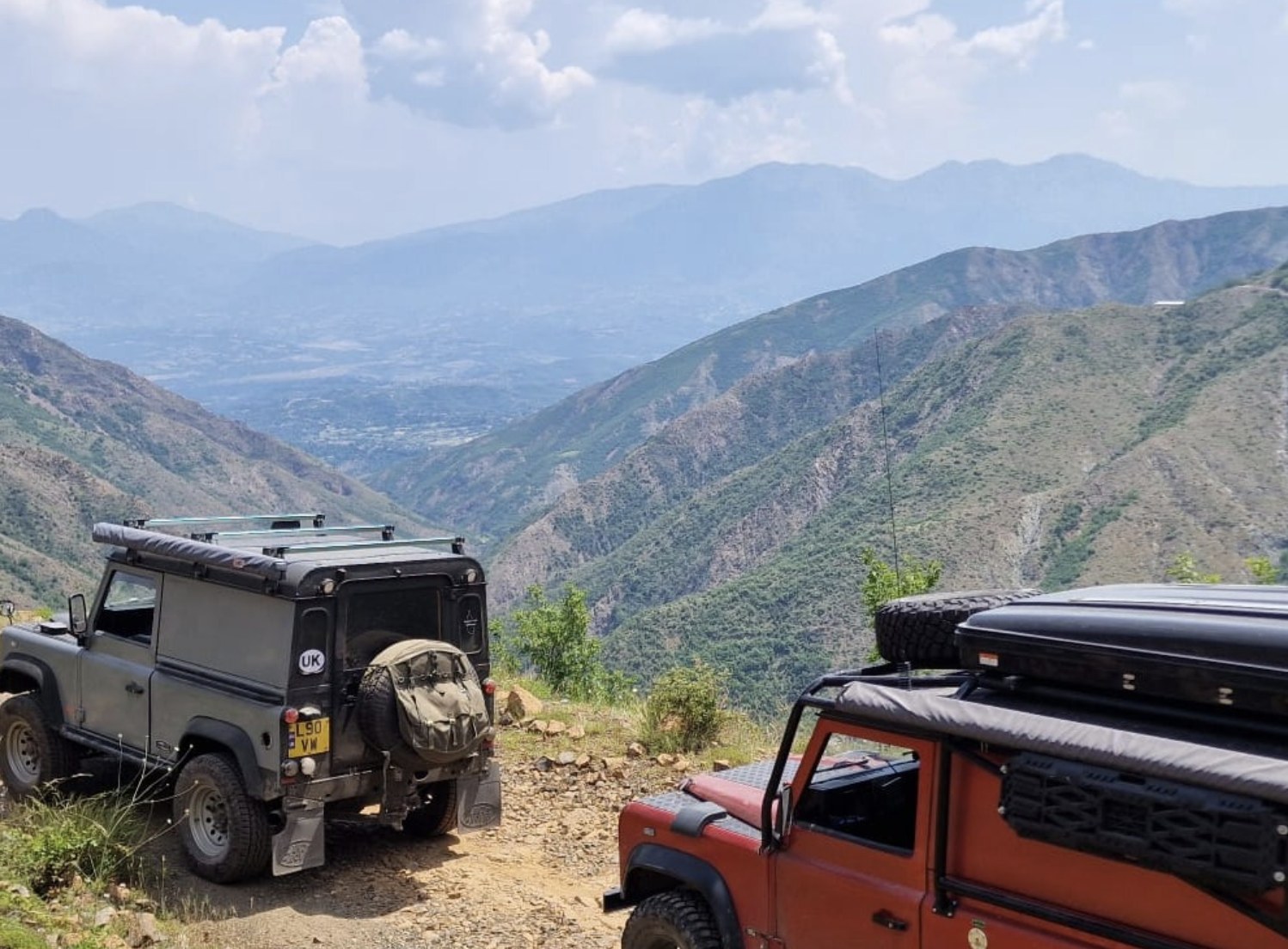 Two Land Rover Defenders parked on a mountain track above a valley in Albania